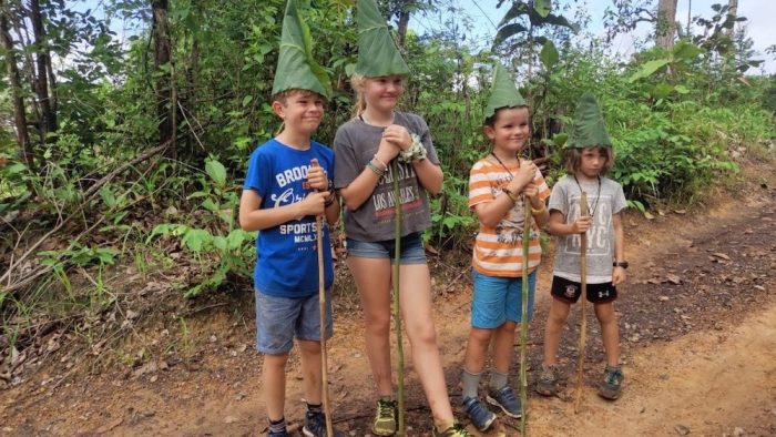Four kids trekking with banana leaf hats family adventure